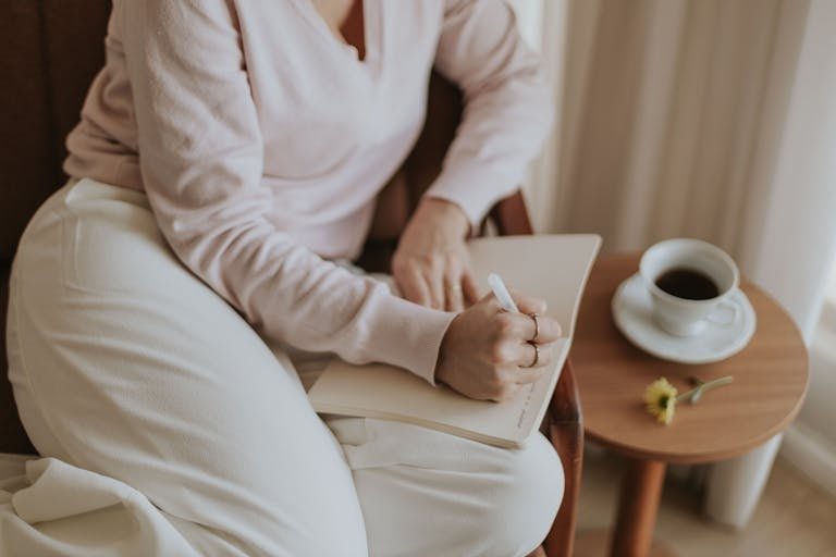A person journaling in a cozy room with a cup of coffee. Warm and inviting atmosphere.