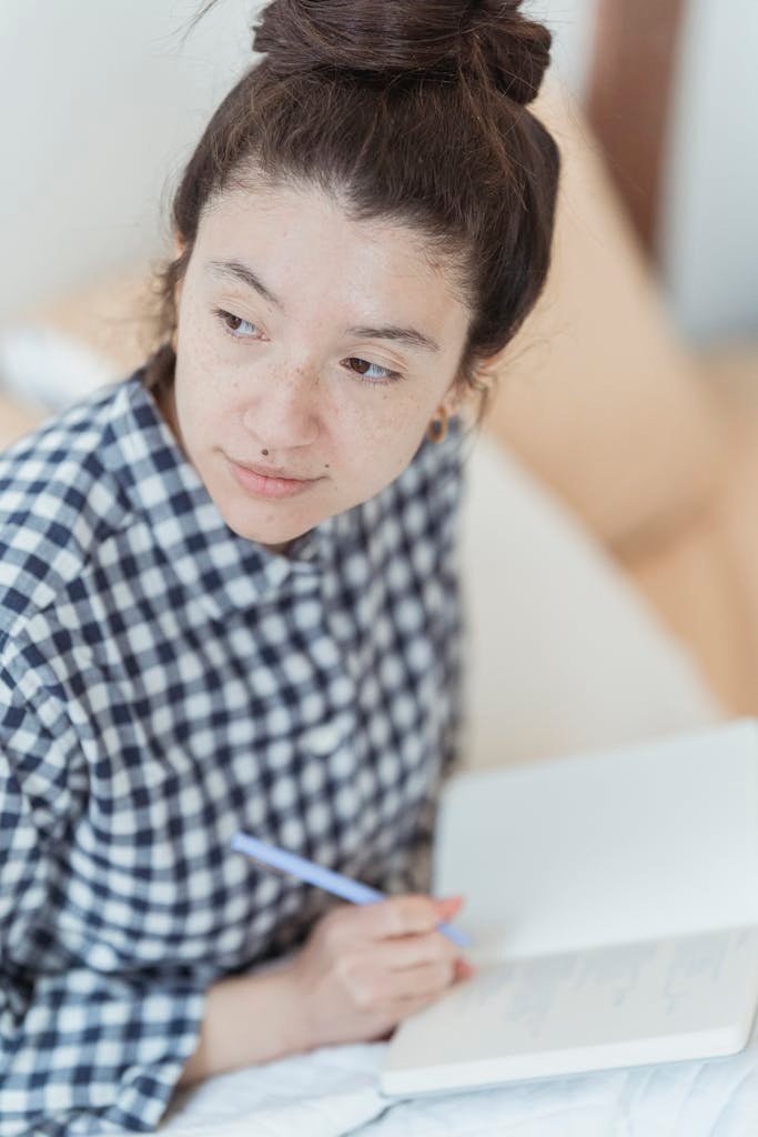 Woman with freckles writing in a notebook, conveying thoughtful reflection and creativity.